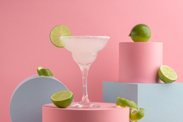 Glass of Margarita cocktail and fresh limes on pink background - obrazy, fototapety, plakaty