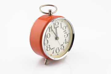 Old orange alarm clock separated on white background. Five minutes to twelve. Analog clock.