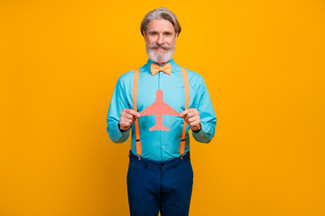 Photo of cool stylish grandpa hold paper air plane recommending choose new airline transportation wear blue shirt suspenders bow tie pants isolated yellow color background
