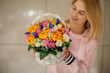 Woman holds in her hands a decorative basket with different spring flowers and looks at it.