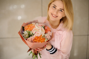 Smiling woman holding a beautiful flower bouquet of fresh roses, peony and ranunculus.