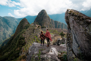 Ein Paar in Ponchos gekleidet, das die Ruinen von Machu Picchu beobachtet