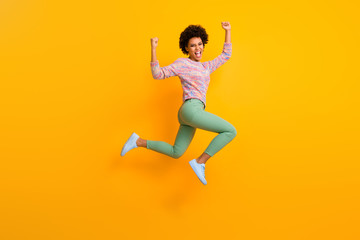 Fototapeta na wymiar Full length photo of delighted crazy athlete afro american girl jump run win marathon raise fists scream yes wear green colorful pants trousers shoes isolated over yellow color background