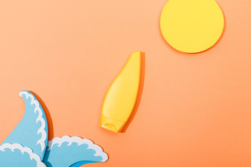 Top view of tube of sunscreen with paper cut sun and sea waves on orange background
