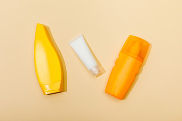 Top view of tubes and dispenser bottle of sunscreen on beige background