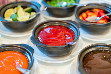 Various bowls of assorted sauces, dips on a asian cuisine buffet