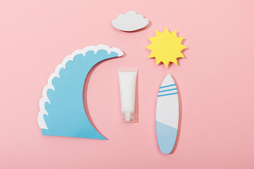 Top view of paper cut sun, cloud, sea wave and surfboard with tube of sunscreen on pink background