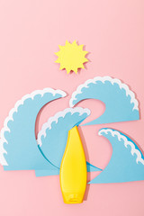 Top view of paper cut sea waves and sun with tube of sunscreen on pink background