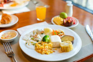 Fresh breakfast table next to window with bread, pastry, egg, fruit, juice, coffee cup