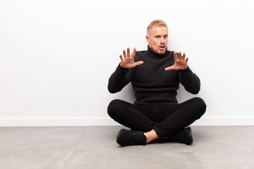 young blonde man feeling terrified, backing off and screaming in horror and panic, reacting to a...