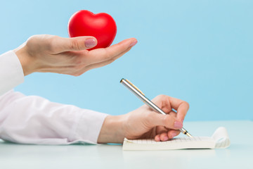 Doctor's hand writes with pen on paper or notebook with a red heart on a blue background. medicine concept, modern technology, cardiologist, heart treatment