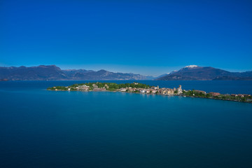Fototapeta na wymiar Sirmione island Lake Garda, Italy. Aerial view. In the background mountains in the snow and blue sky