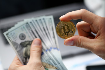 Male hand holds bitcoin and dollar growth on background of laptop keyboard