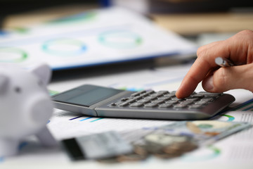 Male hand push key silver calculator is lying on desk cash dollar plots in home office setting....