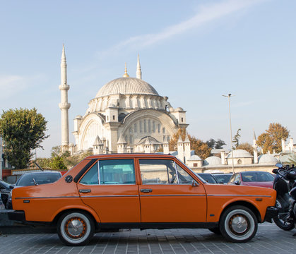 Old classic orange vehicle photographed inside the car park. There is a mosque in the background. Close up.