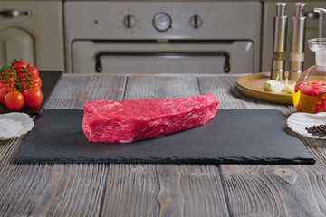 Marbled Beef Steak a rectangular plate of black color ardesia material, on a wooden table. Spices, vegetables on a wooden table. Red hot peppers, cherry tomatoes, garlic.