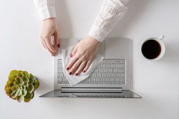 A woman worker cleaning with antivirus wet wipe a laptop and a working office desk before starting...