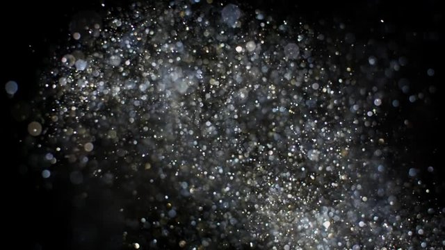 Gold and silver glitter flying after being exploded, bright sparkles bouncing against camera flying and falling down on black background. Top view close up macro slow motion