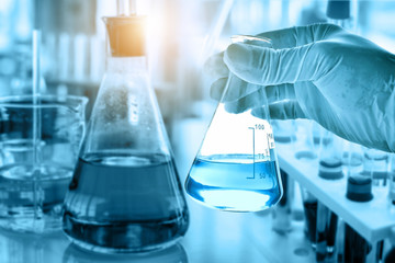 hand of scientist holding flask with lab glassware in chemical laboratory background, science laboratory research and development concept