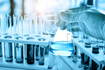 hand of scientist holding flask with lab glassware in chemical laboratory background, science laboratory research and development concept