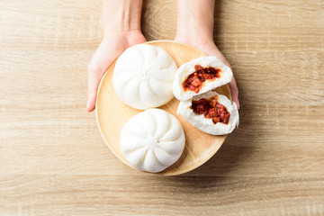 Steamed buns stuffed with red minced pork on wooden plate holding by hand, Asian food, Top view