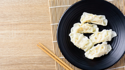 Steamed wonton dumpling stuffed with minced pork and shrimp on black plate and chopsticks, Asian food, Top view