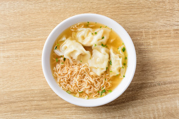 Instant noodles soup and wonton dumpling stuffed with minced pork in a bowl on wooden background, Asian food, Top view