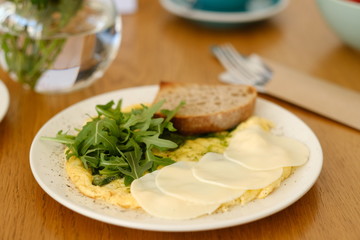 Healthy breakfast in the cafe. Egg omelet with cherry tomatoes decorated with arugula in a white plate on a wooden table. 