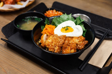 Korean deep fried garlic chicken style with steam rice and fried egg. Served with kimchi in black bowl on black food tray with cold beer. Asian fast food lunch and dining meal.