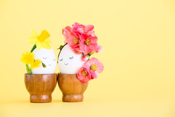 Loving cute couple of Easter eggs with painted faces, decorated with spring and wildflowers on a yellow background.Easter postcard