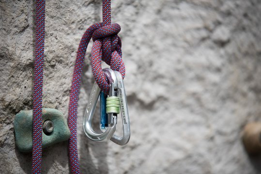 Nahaufnahme von zwei silbernen Karabinerhaken an einem lila farbenen Kletterseil vor einer grauen Kletterwand