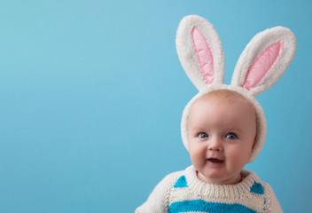 Cute little baby wearing white easter bunny ears against a blue background