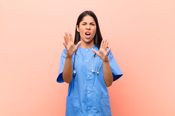 young latin nurse feeling terrified, backing off and screaming in horror and panic, reacting to a...