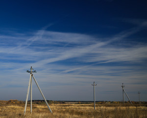 electric poles in an open field against a blue sky