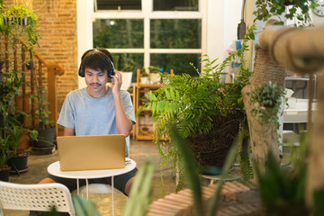 Young man using laptop listening to music on headphone