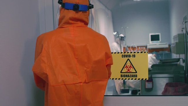 Doctor in an Orange Protective Suit Enters Isolation Room with Coronavirus Patients