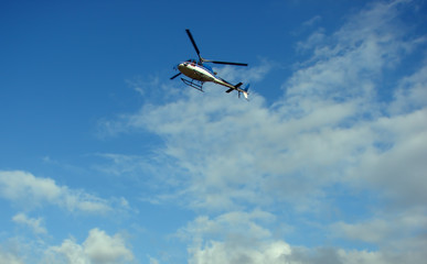 Blue helicopter flying on sky with clouds