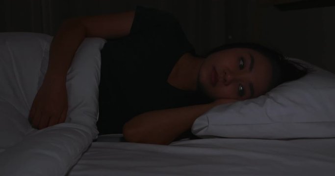 In dark night, beautiful Asian woman try to sleep. That is a late night.