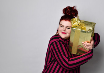 Big ginger woman in striped dress, crown and earrings. Holding golden gift box, looking joyful,...