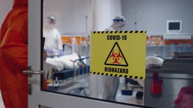 Doctor in an Orange Protective Suit Enters Isolation Room with Coronavirus Patients