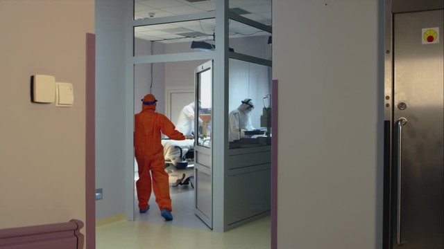 Doctor in an Orange Protective Suit Enters Isolation Room with a Sign Reading Biohazard n the Door