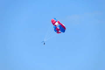 Naklejka na ściany i meble Man flying on a red-blue parachute against a blue sky