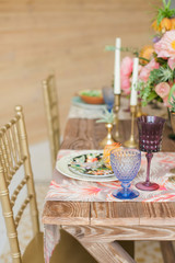 Boho chic style. Decorated wooden table with ceramic plates, cutlery, glasses for drinks, a vase with fresh flowers and candles. Golden chairs. Peonies, Succulents, orchids and Leucospermum.
