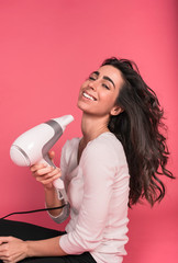 young girl sings with hair dryer isolated on pink background