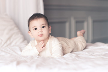 Funny baby boy under 1 year old wearing stylish pajamas lying in bed closeup. Looking at camera. Childhood.