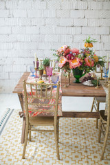 Boho chic style. Decorated wooden table with ceramic plates, cutlery, glasses for drinks, a vase with fresh flowers and candles. Golden chairs. Peonies, Succulents, orchids and Leucospermum.