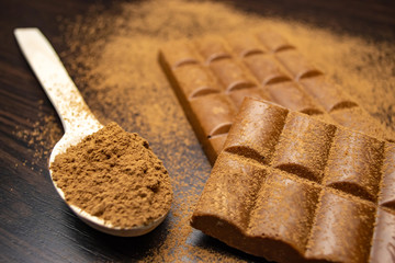 Porous chocolate, wooden spoon with cocoa on a black background