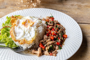 Stir fried minced pork basil with steamed rice and fried egg on a white plate.