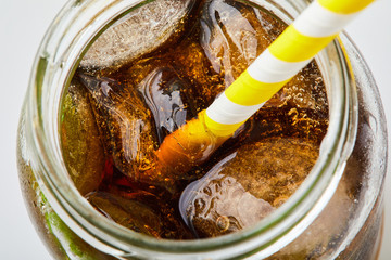 Close up of cola with ice and paper straw in jar, top view. Summer beverage. Disposable stripe...