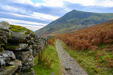 A narrow footpath follows a dry stone wall on one of the walks in The Lake District,Cumbria,UK - 328504954